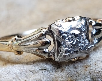 Può includere: Un anello di fidanzamento vintage con un solo diamante incastonato in una montatura in oro bianco. La fascia è in oro giallo e presenta un delicato motivo floreale.
