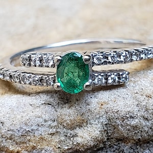 May include: A silver ring with a green emerald gemstone and a band of small diamonds.