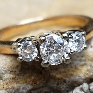May include: A gold band ring with three round diamonds. The center diamond is larger than the two side diamonds.