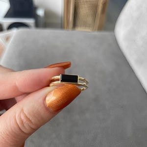 Pode incluir: Um anel de ouro com uma pedra retangular preta engastada no centro. O anel é de design de banda dupla.