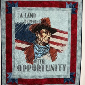 May include: A blue and red quilt with a cowboy and an American flag. The quilt has the text "A Land Brimming With Opportunity".