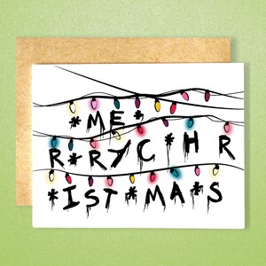 Puede incluir: Una tarjeta blanca con una ilustración en blanco y negro de luces navideñas que deletrean "Feliz Navidad". Las luces son de diferentes colores, incluyendo rojo, amarillo, azul, rosa y verde.