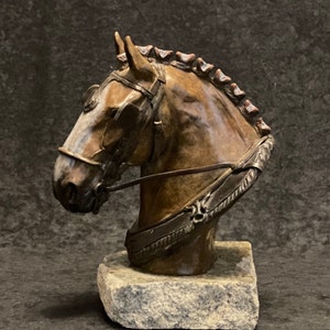 Puede incluir: Escultura de bronce de la cabeza de un caballo con un arn&eacute;s, montada sobre una base de piedra.