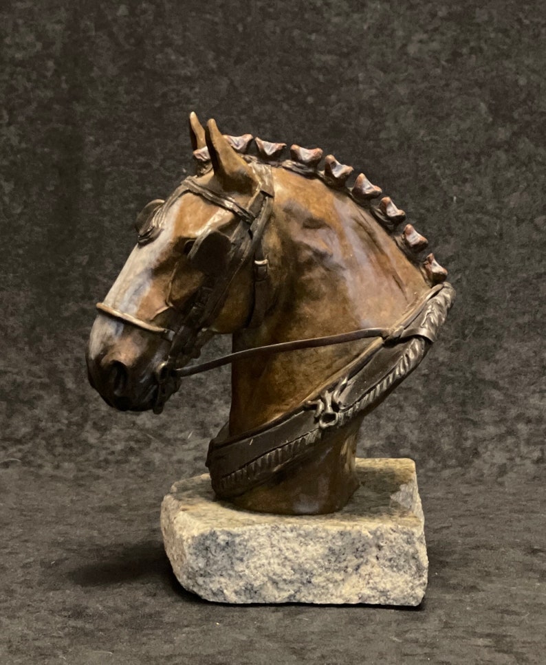 Puede incluir: Escultura de bronce de la cabeza de un caballo con un arn&eacute;s, montada sobre una base de piedra.