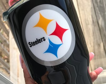 May include: Black stainless steel tumbler with a white, silver, red, yellow, and blue Pittsburgh Steelers logo. The logo says "Steelers".