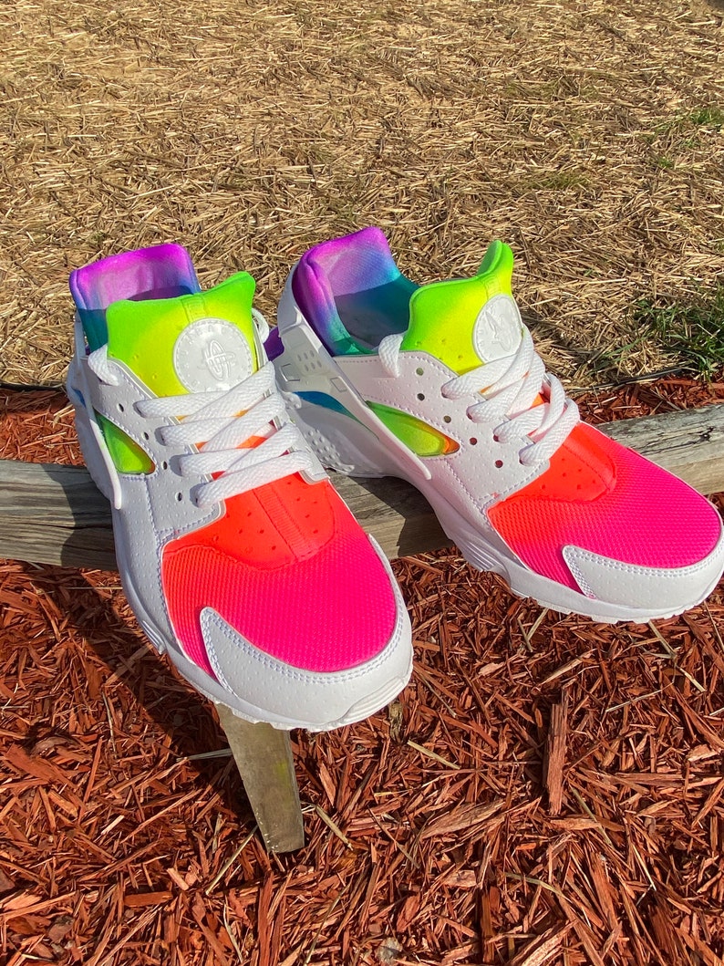May include: White Nike Air Huarache sneakers with a rainbow ombre design on the back of the shoe and a pink and orange ombre design on the front of the shoe.