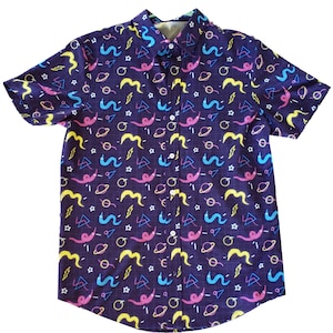 May include: Short-sleeved button-down shirt with a dark purple background and a colorful pattern. The pattern includes yellow, pink, blue, and white shapes, including squiggles, planets, and lightning bolts. The shirt has a classic collar and white buttons.