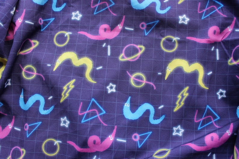 May include: Dark purple fabric with a repeating pattern of colorful worms, planets, stars, lightning bolts, and geometric shapes. The design features neon colors on a grid background.
