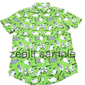 Puede incluir: Camisa de manga corta con un fondo verde vibrante. La camisa está cubierta con un patrón repetido de ratones de dibujos animados blancos y grises, con detalles en negro. El texto "zealii sample" está impreso en la camisa.