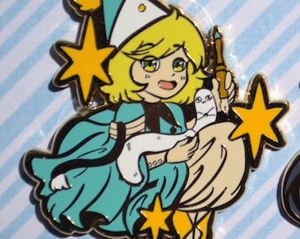 May include: Two enamel pins featuring anime-style characters. The left pin shows a blonde character in a teal robe and hat holding a small white creature. The right pin shows a white-haired character in a beige robe reading a blue book.