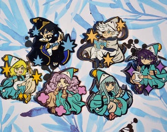 May include: A collection of six enamel pins featuring stylized characters in wizard-like attire, each with distinct hair colors, robes, and accessories like books or stars, arranged in a group on a light blue and white leaf-patterned surface.