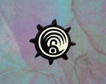May include: A circular black and white enamel pin featuring a central graphic of an open padlock surrounded by concentric semicircular lines. The pin has a spiked outer edge with eight pointed protrusions extending from the circular frame.