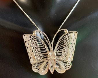 Pode incluir: Um colar de prata com um pingente de borboleta. A borboleta é intrincadamente detalhada e tem um delicado design de filigrana.