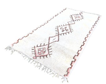 May include: A white rug with a pink and brown geometric pattern. The rug has fringe on all sides.
