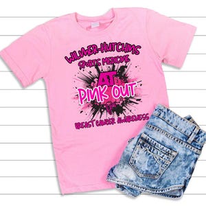 May include: Pink t-shirt with a black and pink graphic that says "Wilmer-Hutchins Sports Medicine AT Pink Out for Breast Cancer Awareness".