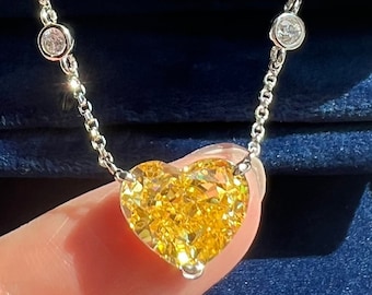 May include: A delicate silver chain necklace with a large, heart-shaped yellow diamond pendant. The necklace is displayed in a blue velvet box.
