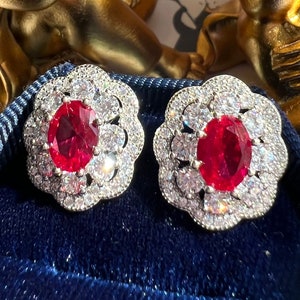 May include: A pair of silver earrings with a red gemstone surrounded by smaller white gemstones. The earrings are in a blue velvet box.