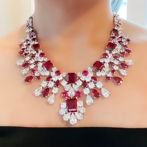 May include: A statement necklace with a large, central ruby surrounded by smaller rubies and diamonds. The necklace is made of silver and has a delicate, feminine design.