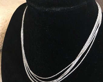 May include: A silver multi-strand necklace with a delicate chain design. The necklace is displayed on a black velvet mannequin.