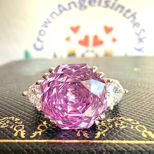 May include: A silver ring with a large, faceted, purple gemstone surrounded by two smaller, clear gemstones.