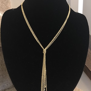 May include: A gold necklace with a tassel design. The necklace is made of multiple strands of chain and has small gold beads at the end of the tassel.