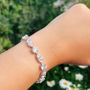 May include: A silver bracelet with a row of clear, oval-shaped stones. The bracelet is on a person's wrist.