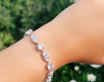 May include: A silver bracelet with a row of clear, oval-shaped stones. The bracelet is on a person's wrist.
