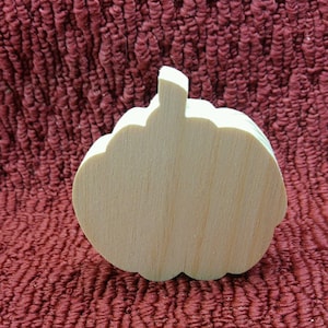 May include: A plain, unfinished wooden pumpkin cutout. The pumpkin is a light brown color and has a smooth surface.