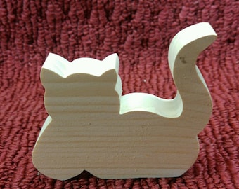 May include: A wooden cutout of a cat in a sitting position. The cat is made of light-colored wood and has a simple, cartoon-like design.