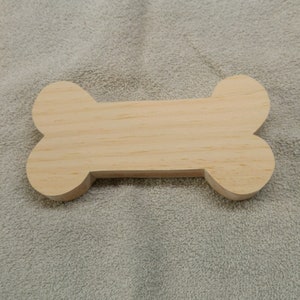 May include: A plain, unfinished wooden bone shape. The bone is light brown and has a smooth surface.