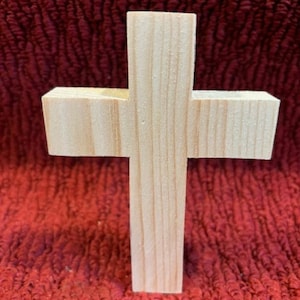 May include: A simple wooden cross made of light-coloured wood. The cross is standing upright on a red surface.