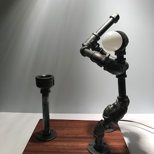 Puede incluir: Una lámpara de metal negro con forma de jugador de béisbol, con una bombilla blanca, de pie sobre una base de madera.