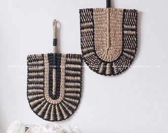 May include: Two black and natural woven wall decor fans with a black hanging loop. The fans are in the shape of a half circle with a black and natural woven pattern.