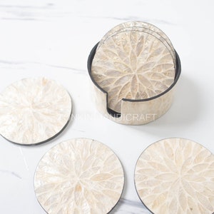 May include: Set of six white mother of pearl coasters with a floral design. The coasters are in a round holder with a black rim.