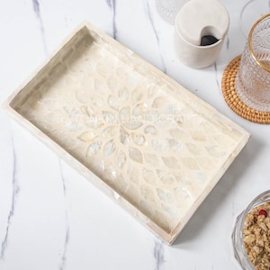 May include: A rectangular tray made of white mother of pearl with a floral design. The tray is on a white marble surface.