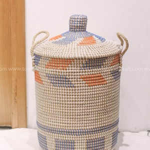 May include: A woven storage basket with a lid, featuring a geometric pattern in blue and orange. The basket is made of natural materials and has two rope handles.