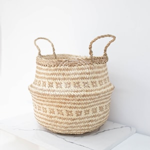 Könnte beinhalten: Ein geflochtener Seegras-Korb mit zwei Griffen. Der Korb hat ein geometrisches Muster und ist hellbraun.