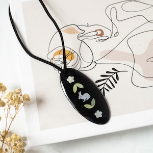 May include: Black oval pendant necklace with a rabbit and floral design. The pendant is on a black cord. The text "TONKIN HANDICRAFT" is visible in the upper right corner.