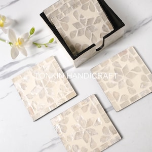 May include: Set of four white mother of pearl coasters with a floral design. The coasters are in a wooden holder.