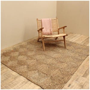 May include: A natural fiber rug with a woven pattern in a light brown color. A light pink throw is draped over a wooden chair with a woven seat.