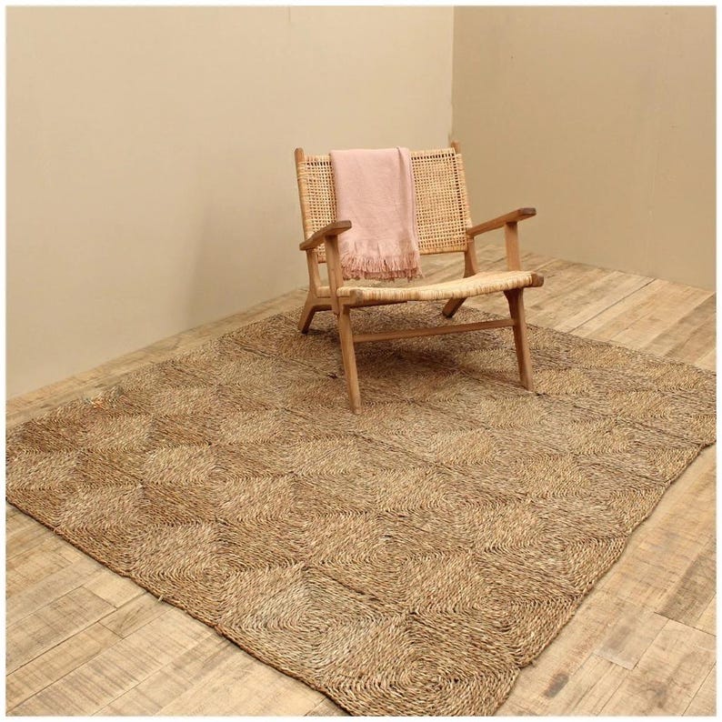 May include: A natural fiber rug with a woven pattern in a light brown color. A light pink throw is draped over a wooden chair with a woven seat.