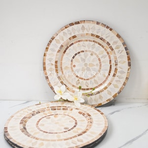 Könnte beinhalten: Zwei runde, weiße und braune Dekorationsplatten aus Mosaikfliesen. Die Platten sind übereinander gestapelt. Die obere Platte hat ein florales Design in der Mitte.