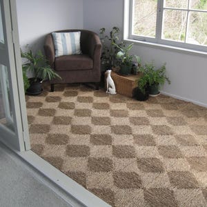 May include: A brown armchair with a blue and white patterned cushion sits in a room with a checkered brown and white floor. A white ceramic dog figurine sits on the floor in front of the chair.