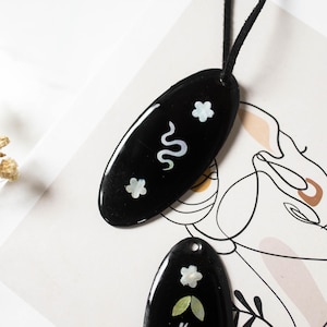 Könnte beinhalten: Eine weiße Keramik-Tasse mit schwarzem Henkel und dem Text "But First, Coffee" in fetter, schwarzer Schrift. Die Tasse steht vor einem verschwommenen Hintergrund, der eine gemütliche Umgebung suggeriert.