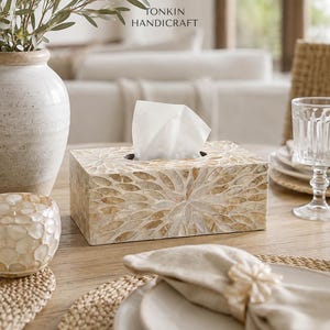 May include: A rectangular tissue box cover featuring a mosaic pattern of iridescent, petal-shaped shell pieces in shades of cream and tan. The box has a central oval opening with a white tissue protruding from the top. The text TONKIN HANDICRAFT is visible.