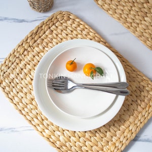 Puede incluir: Un plato blanco con dos pequeñas frutas naranjas y un tenedor y una cuchara sobre un mantel individual tejido. El mantel individual está hecho de materiales naturales y tiene un color marrón claro.