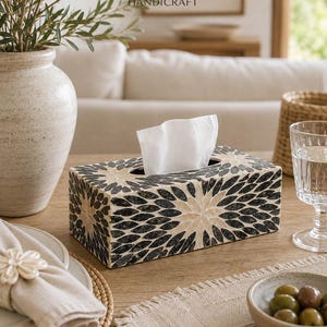 May include: A rectangular tissue box cover featuring a decorative inlay pattern of dark charcoal and cream-colored petal shapes arranged in a radial floral design. The box has a central oval opening with a white tissue protruding from the top.