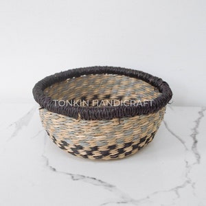 Pode incluir: Uma cesta tecida com uma borda preta e um padrão xadrez em tons de cinza e preto. A cesta está sentada em uma superfície de mármore branco. O texto "TONKIN HANDICRAFT" é visível na cesta.