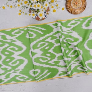 May include: Green and white ikat fabric with a yellow border. The fabric is folded in half and has a white background with green swirls.