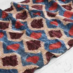 May include: A fabric with a geometric pattern in shades of blue, red, brown, and beige. The fabric has a textured, almost velvet-like surface.